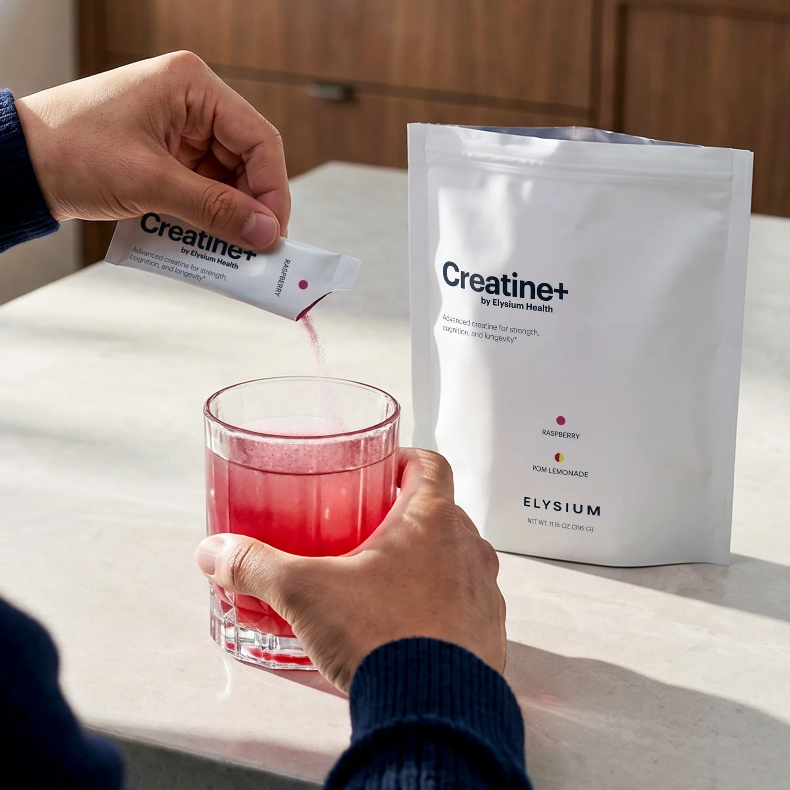 A person pouring a raspberry Creatine+ stick into a glass of water on a kitchen counter