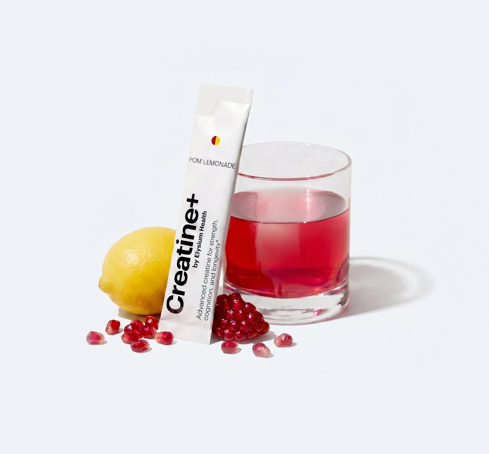 Pomegranate lemonade Creatine+ stick beside a prepared drink, pomegranate, and lemon
