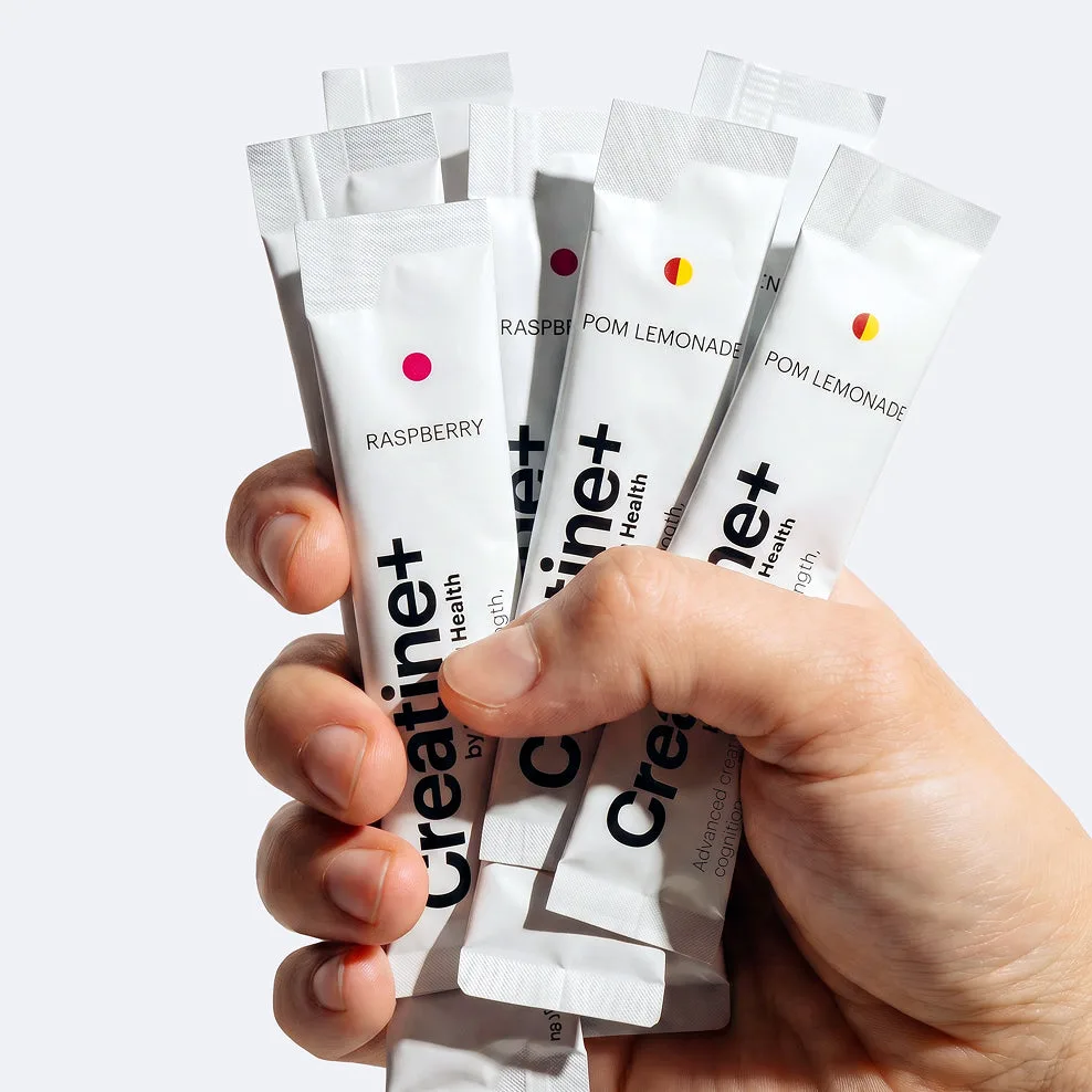 A hand holding several individually packed Creatine+ daily sticks